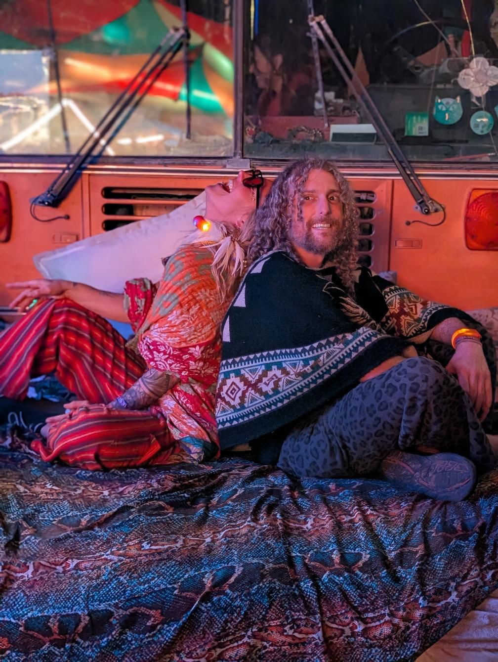 Holy Wild Music artists seated together in colorful night lighting beside The Magic Fool Bus